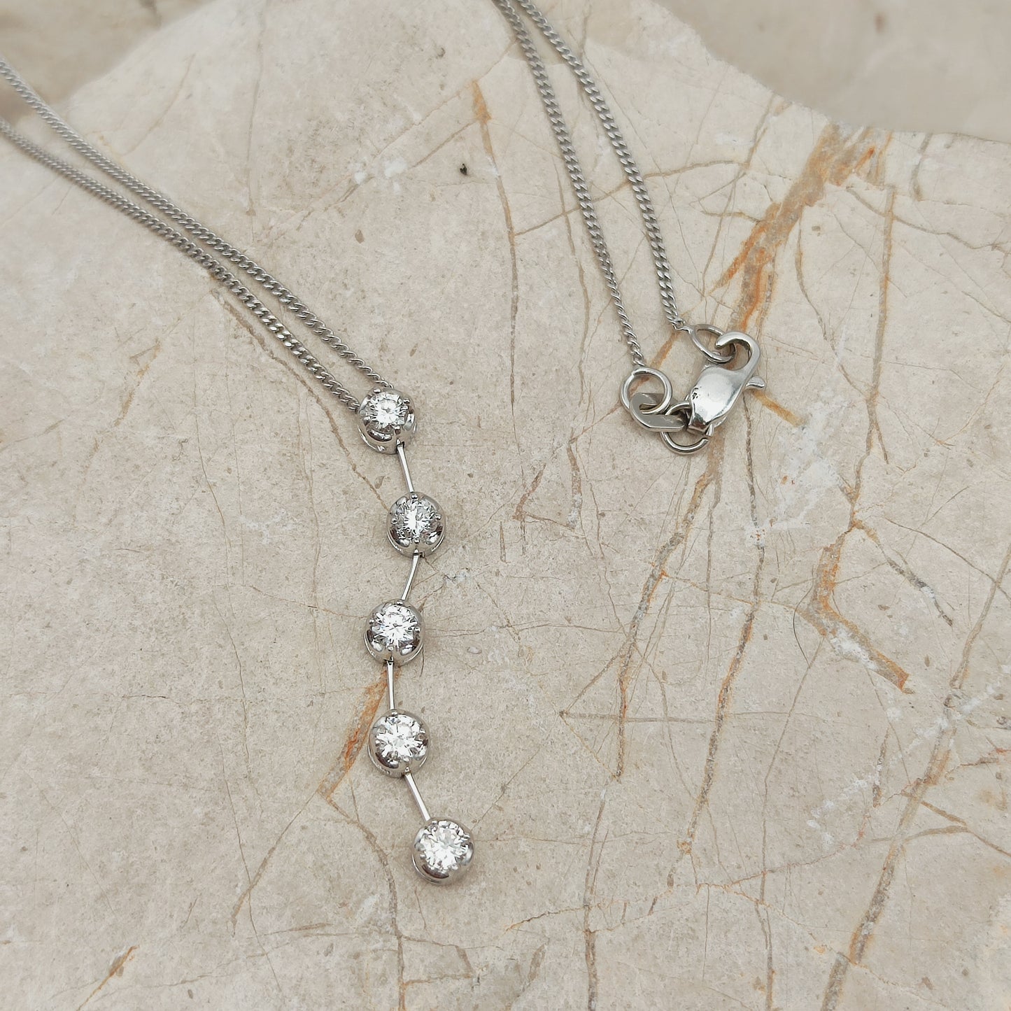Detail van vintage witgouden hanger met vijf diamanten onder elkaar