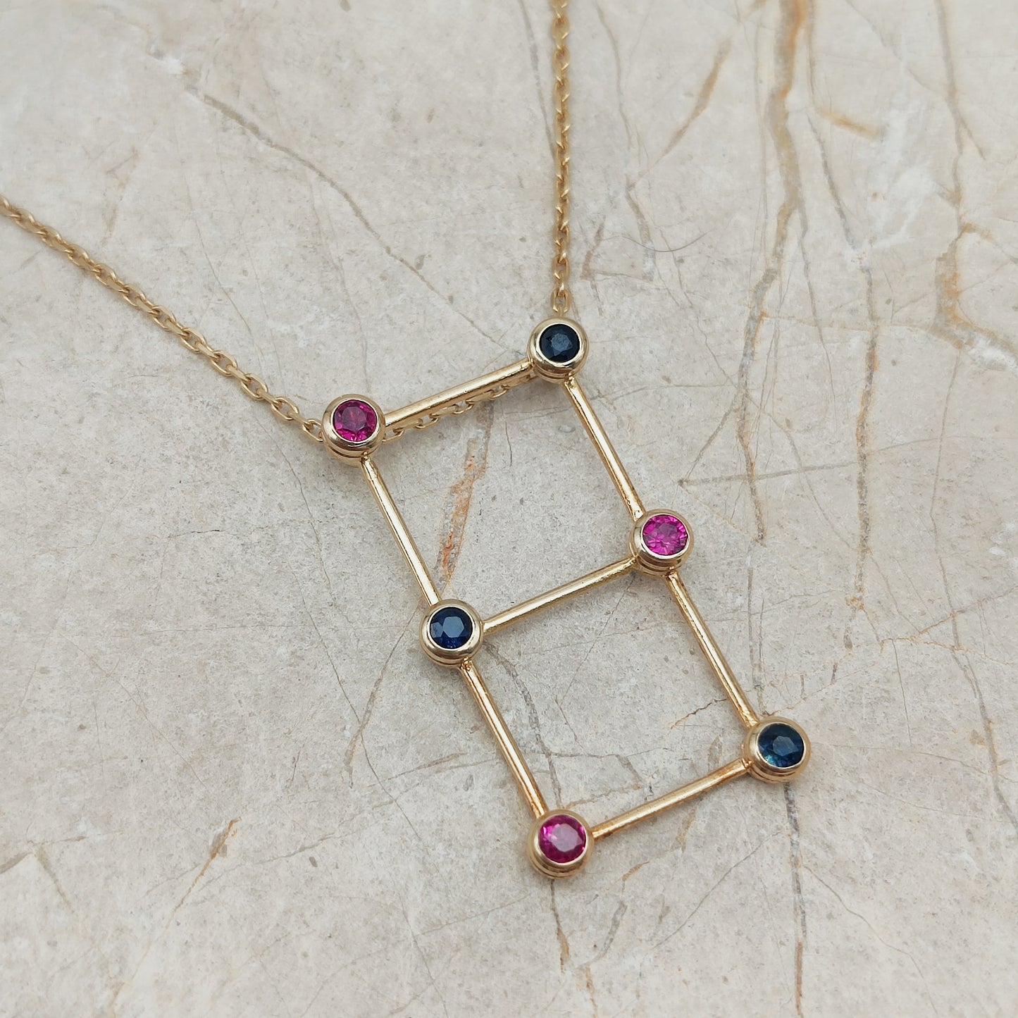 Detail van gouden laddervormige hanger met robijnen en blauwe saffieren in gesloten zetkasten