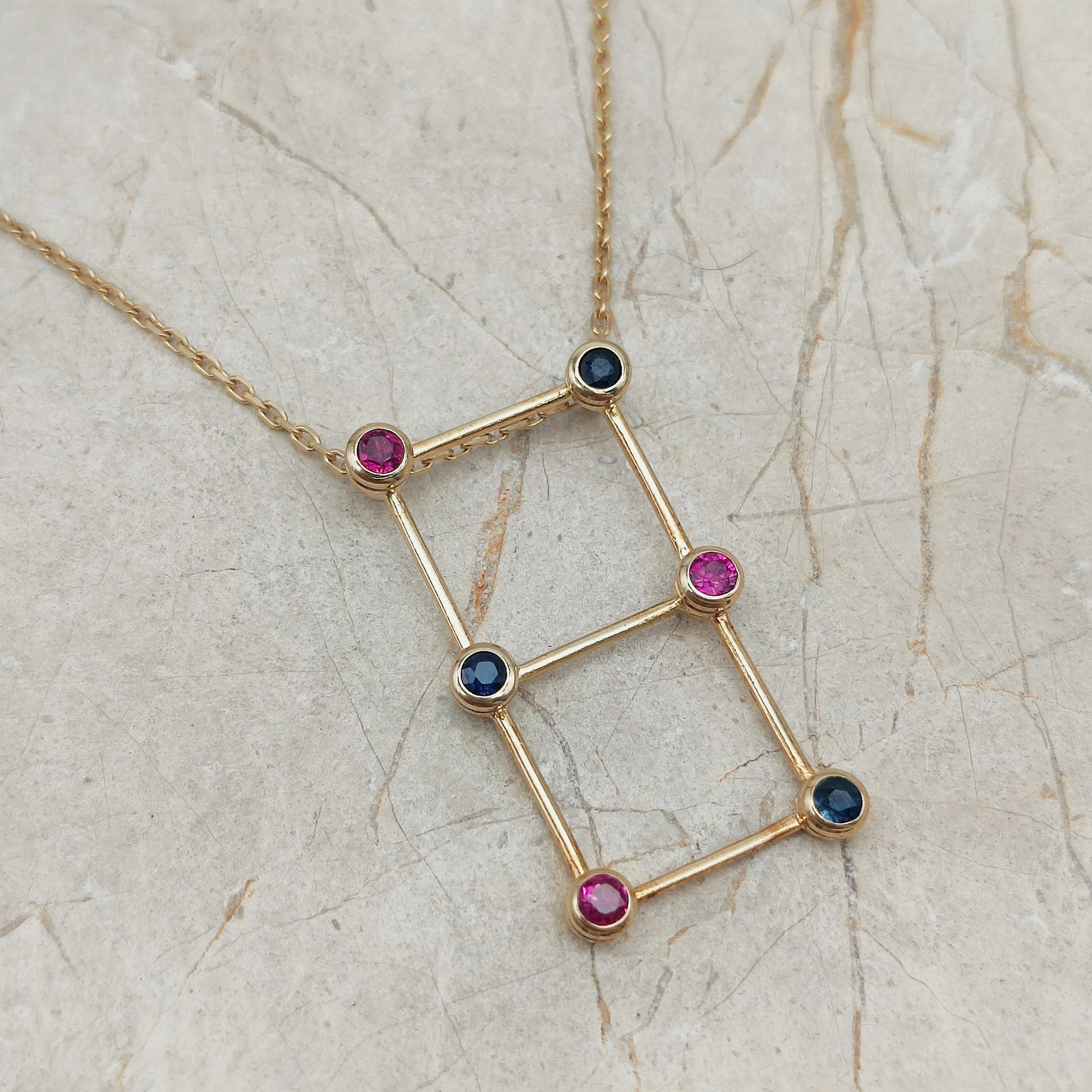Detail van gouden laddervormige hanger met robijnen en blauwe saffieren in gesloten zetkasten