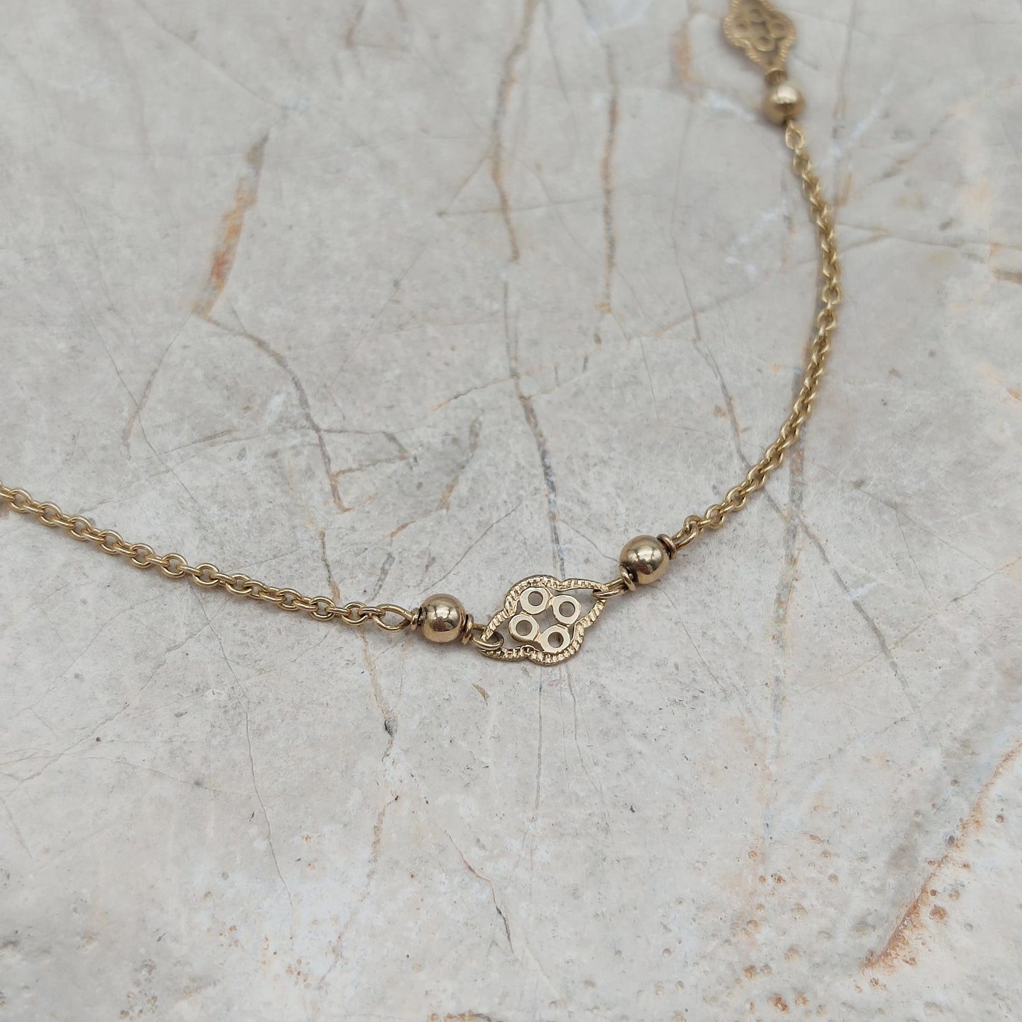 Detail van gouden ketting met decoratief tussenstukje en bolletjes