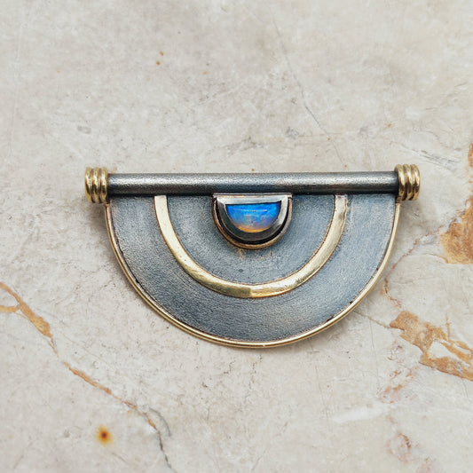 Geometrische halfronde broche in donker zilver met gouden lijnen en een blauw oplichtende opaal