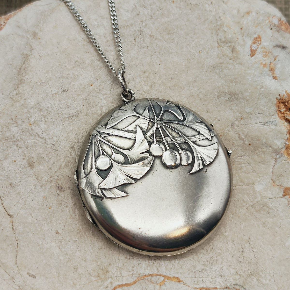 Antiek Art Nouveau-medaillon in 800 zilver met ginkgobladeren en vruchten in reliëf, aan een zilveren ketting.