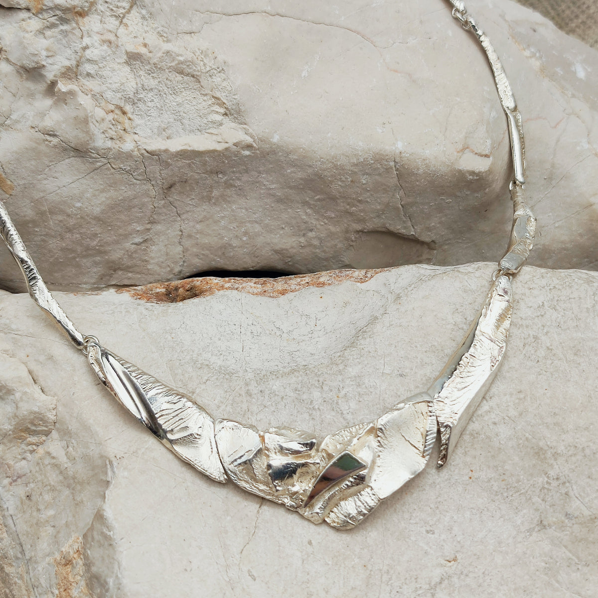 Finse AKT-halsketting in sterling zilver met gebogen schakels en een abstract middenstuk in hoogglans en grillig reliëf.