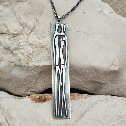 Lange brutalistische sterling zilveren hanger van Mies De Wilde met een gestileerde man en vrouw, aan een zwarte Zancan-ketting.