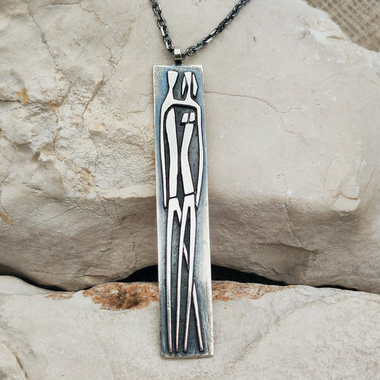 Lange brutalistische sterling zilveren hanger van Mies De Wilde met een gestileerde man en vrouw, aan een zwarte Zancan-ketting.